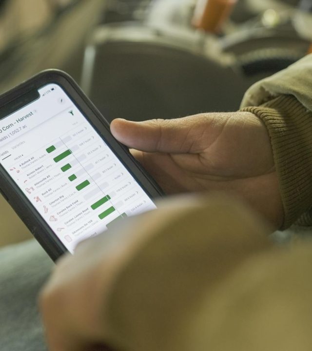 Close-up of a person in winter clothing analyzing farming data on a smartphone screen.